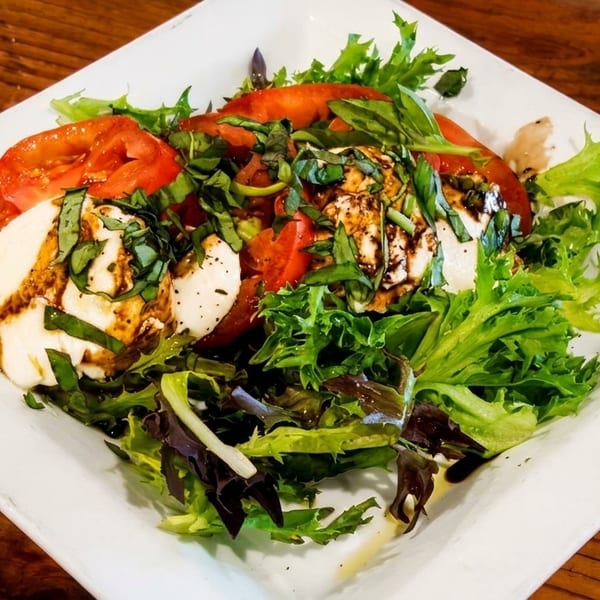 Caprese salad with fresh mozzarella, sliced tomatoes, basil, and balsamic glaze on a white plate.