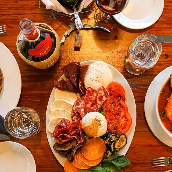 Overhead view of a wooden table with chicken, charcuterie, seafood stew, and Chianti wine.