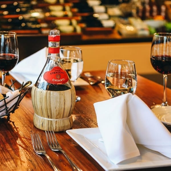 A rustic wooden table set with a Chianti wine bottle, bread basket, and wine glasses.