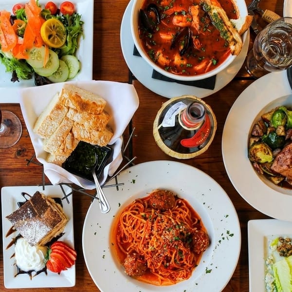 A wooden table laden with various Italian dishes, including pasta, seafood stew, salads, and charcuterie.