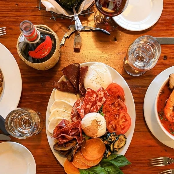 Overhead view of a rustic wooden table laden with Italian dishes, including seafood stew, charcuterie, and roasted vegetables.