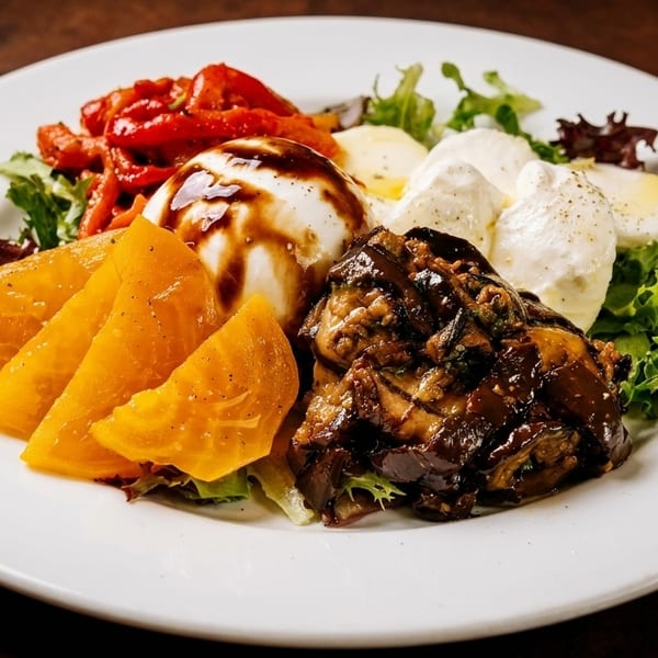 A white plate with burrata, roasted red peppers, golden beets, and eggplant caponata on lettuce.