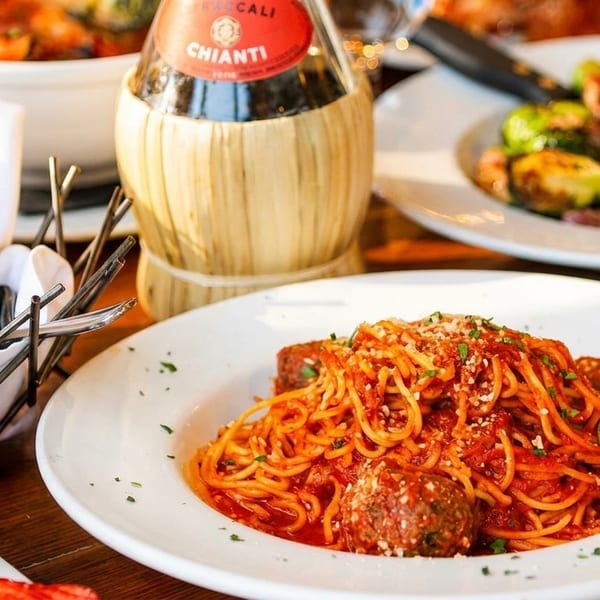 Spaghetti and meatballs, bread basket, and Chianti bottle on a wooden table.