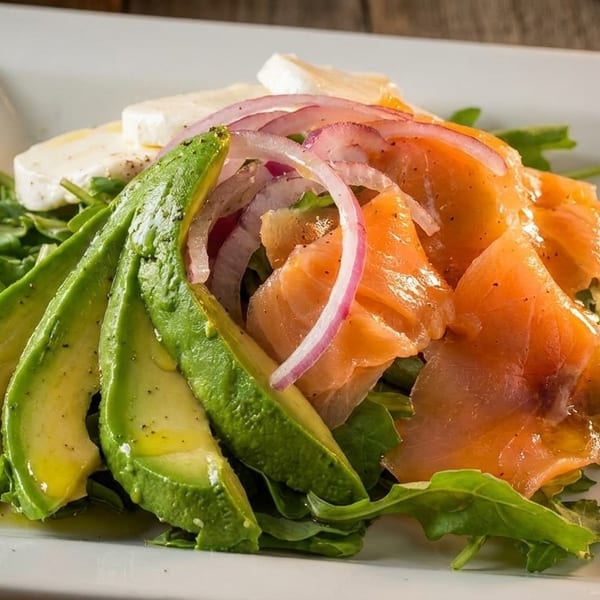 A fresh salad with sliced avocado, smoked salmon, red onion, and mozzarella on a bed of arugula.