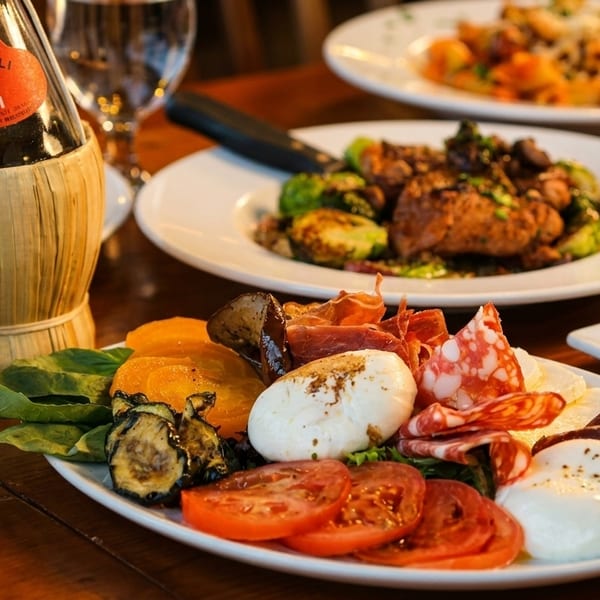 Italian meal with Chianti wine, charcuterie, pasta, and roasted vegetables on a wooden table.